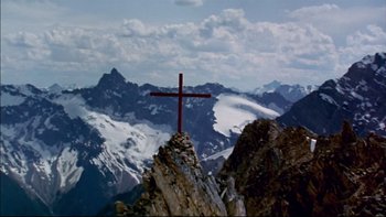 Movie still from “Alive” (1993), directed by Frank Marshall – A cross on top of a mountain with a sky background; Extreme Wide shot, Low angle