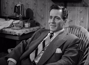 Movie still from “All About Eve” (1950), directed by Joseph L. Mankiewicz – A man in a suit and tie sitting in a chair; Medium shot, Low angle