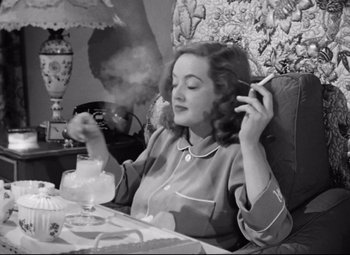 Movie still from “All About Eve” (1950), directed by Joseph L. Mankiewicz – A black and white photo of a woman smoking a cigarette; Medium shot, High angle