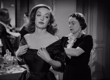 Movie still from “All About Eve” (1950), directed by Joseph L. Mankiewicz – A woman is helping another woman put on a dress; Medium shot, Over the shoulder angle