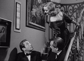 Movie still from “All About Eve” (1950), directed by Joseph L. Mankiewicz – Two men and a woman sitting on the stairs of a house; Medium shot, Low angle