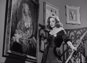 Movie still from “All About Eve” (1950), directed by Joseph L. Mankiewicz – A black and white photo of a woman standing in front of a painting; Medium shot, Low angle