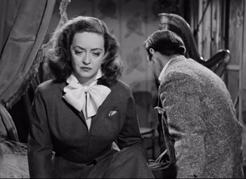 Movie still from “All About Eve” (1950), directed by Joseph L. Mankiewicz – A woman sitting on a chair next to a man in a suit; Close Up shot, Over the shoulder angle