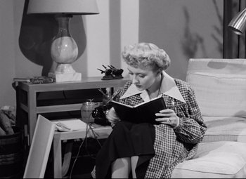 Movie still from “All About Eve” (1950), directed by Joseph L. Mankiewicz – An old photo of a woman sitting on a chair reading a book; Medium shot, High angle