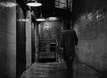 Movie still from “All About Eve” (1950), directed by Joseph L. Mankiewicz – A man walking down a hallway in a dark building; Wide shot, High angle