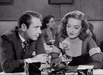 Movie still from “All About Eve” (1950), directed by Joseph L. Mankiewicz – A man and a woman sitting at a table with drinks; Medium shot, High angle