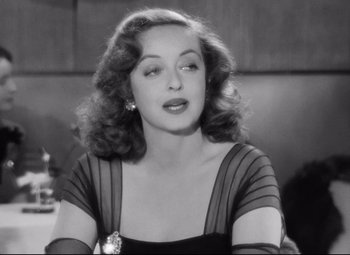 Movie still from “All About Eve” (1950), directed by Joseph L. Mankiewicz – A black - and - white photo of a woman in a black dress; Close Up shot, Over the shoulder angle