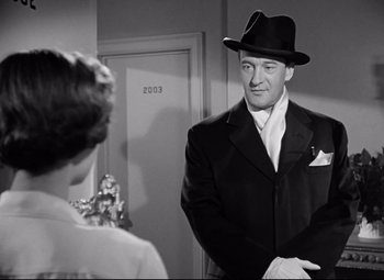 Movie still from “All About Eve” (1950), directed by Joseph L. Mankiewicz – A black and white photo of a man in a suit and a hat; Medium shot, Over the shoulder angle