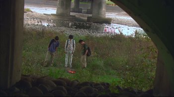 Movie still from “All About Lily Chou-Chou” (2001), directed by Shunji Iwai – A group of people standing in the grass near a river; Extreme Wide shot, High angle