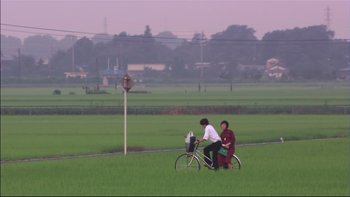 Movie still from “All About Lily Chou-Chou” (2001), directed by Shunji Iwai – Two people on a bicycle in a field; Extreme Wide shot, High angle