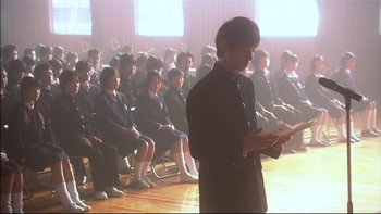 Movie still from “All About Lily Chou-Chou” (2001), directed by Shunji Iwai – A man standing in front of a group of people; Medium shot, Low angle