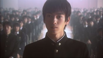Movie still from “All About Lily Chou-Chou” (2001), directed by Shunji Iwai – A young man in a black jacket is in front of a group of people; Close Up shot, Low angle