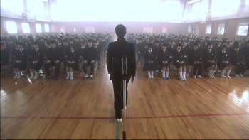 Movie still from “All About Lily Chou-Chou” (2001), directed by Shunji Iwai – A man standing in front of a group of people; Extreme Wide shot, High angle