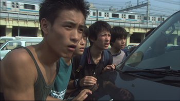 Movie still from “All About Lily Chou-Chou” (2001), directed by Shunji Iwai – A group of young men standing next to each other on the side of the road; Close Up shot, Low angle