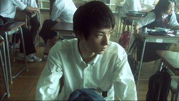 Movie still from “All About Lily Chou-Chou” (2001), directed by Shunji Iwai – A young man sitting in front of a group of people; Close Up shot, Low angle