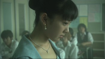 Movie still from “All About Lily Chou-Chou” (2001), directed by Shunji Iwai – A woman with a necklace and earrings in front of a group of people; Close Up shot, Low angle