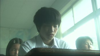 Movie still from “All About Lily Chou-Chou” (2001), directed by Shunji Iwai – A young man sitting in front of an open book; Close Up shot, Low angle