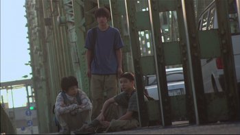 Movie still from “All About Lily Chou-Chou” (2001), directed by Shunji Iwai – A group of young men sitting on the ground next to each other; Wide shot, Low angle