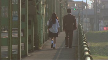 Movie still from “All About Lily Chou-Chou” (2001), directed by Shunji Iwai – A man and a woman walking down a sidewalk; Wide shot, Low angle