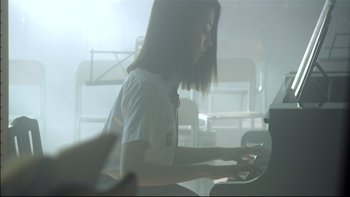 Movie still from “All About Lily Chou-Chou” (2001), directed by Shunji Iwai – A girl is playing the piano in a dimly - lit room; Medium shot, Low angle