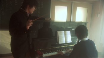 Movie still from “All About Lily Chou-Chou” (2001), directed by Shunji Iwai – A boy is playing the piano while another boy watches; Medium shot, Low angle