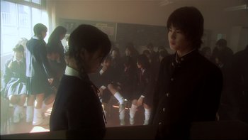 Movie still from “All About Lily Chou-Chou” (2001), directed by Shunji Iwai – Two young girls in school uniforms standing next to each other in a classroom; Medium shot, Over the shoulder angle