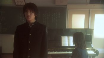 Movie still from “All About Lily Chou-Chou” (2001), directed by Shunji Iwai – A man standing in front of a piano in a room; Medium shot, Low angle