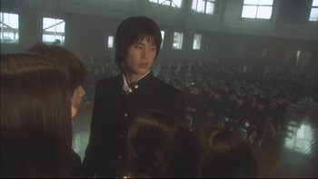 Movie still from “All About Lily Chou-Chou” (2001), directed by Shunji Iwai – A man standing in front of a crowd of people; Medium shot, Low angle