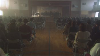 Movie still from “All About Lily Chou-Chou” (2001), directed by Shunji Iwai – A group of people sitting in chairs in front of an audience; Extreme Wide shot, High angle