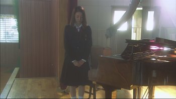 Movie still from “All About Lily Chou-Chou” (2001), directed by Shunji Iwai – A girl in a school uniform is standing in front of a piano; Medium shot, Low angle