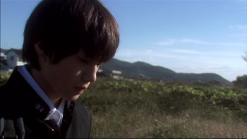 Movie still from “All About Lily Chou-Chou” (2001), directed by Shunji Iwai – A young boy in a suit and tie in a grassy field; Close Up shot, Low angle
