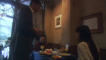 Movie still from “All About Lily Chou-Chou” (2001), directed by Shunji Iwai – A man standing at a table in front of two women; Medium shot, Over the shoulder angle