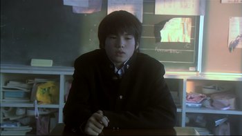 Movie still from “All About Lily Chou-Chou” (2001), directed by Shunji Iwai – A young man sitting at a table in front of a window; Medium shot, Low angle