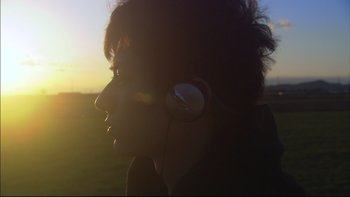 Movie still from “All About Lily Chou-Chou” (2001), directed by Shunji Iwai – A person with headphones in a field at sunset; Close Up shot, Low angle