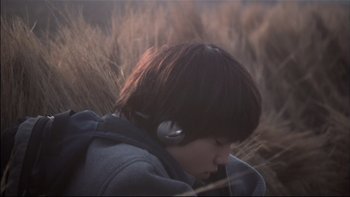 Movie still from “All About Lily Chou-Chou” (2001), directed by Shunji Iwai – A young boy wearing headphones in a field of tall grass; Close Up shot, High angle