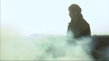 Movie still from “All About Lily Chou-Chou” (2001), directed by Shunji Iwai – A man with headphones standing next to a body of water; Medium shot, Low angle
