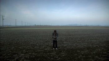 Movie still from “All About Lily Chou-Chou” (2001), directed by Shunji Iwai – A person standing in a field with a cell phone; Extreme Wide shot, Low angle