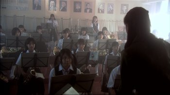 Movie still from “All About Lily Chou-Chou” (2001), directed by Shunji Iwai – A group of people sitting in a room with musical instruments; Wide shot, Over the shoulder angle
