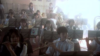 Movie still from “All About Lily Chou-Chou” (2001), directed by Shunji Iwai – A group of young people playing musical instruments in a room; Extreme Wide shot, Low angle