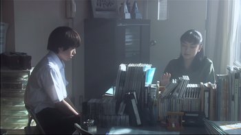 Movie still from “All About Lily Chou-Chou” (2001), directed by Shunji Iwai – A man and a woman sitting in front of a desk; Medium shot, Over the shoulder angle