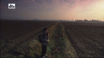 Movie still from “All About Lily Chou-Chou” (2001), directed by Shunji Iwai – A person standing in a field with a backpack; Extreme Wide shot, Low angle