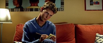 Movie still from “All About My Mother” (1999), directed by Pedro Almodóvar – A man sitting on a couch writing on a piece of paper; Close Up shot, Low angle