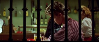 Movie still from “All About My Mother” (1999), directed by Pedro Almodóvar – A man writing on a piece of paper in front of a glass of orange juice; Medium shot, Over the shoulder angle