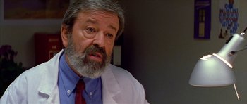 Movie still from “All About My Mother” (1999), directed by Pedro Almodóvar – An older man in a white lab coat and a red tie; Close Up shot, Low angle