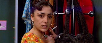 Movie still from “All About My Mother” (1999), directed by Pedro Almodóvar – A woman smoking a cigarette while wearing a colorful dress; Close Up shot, Over the shoulder angle