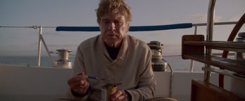 Movie still from “All Is Lost” (2013), directed by J.C. Chandor – An older man sitting on top of a sailboat eating; Close Up shot, Low angle