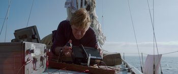 Movie still from “All Is Lost” (2013), directed by J.C. Chandor – An older woman is working on a radio; Medium shot, Low angle