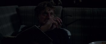 Movie still from “All Is Lost” (2013), directed by J.C. Chandor – A man sitting on a couch holding a book; Close Up shot, Over the shoulder angle
