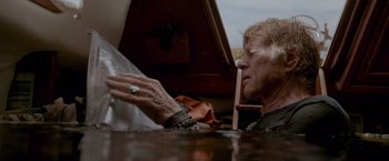 Movie still from “All Is Lost” (2013), directed by J.C. Chandor – An older woman sitting at a table looking at something on the table; Close Up shot, Low angle