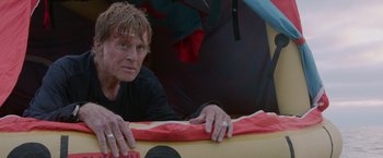 Movie still from “All Is Lost” (2013), directed by J.C. Chandor – An older man leaning on a surfboard in the water; Close Up shot, High angle